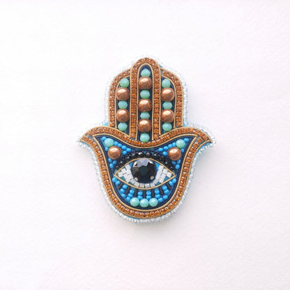 A handcrafted piece of jewelry featuring a blue and gold design with a large eye-shaped gemstone in the center.