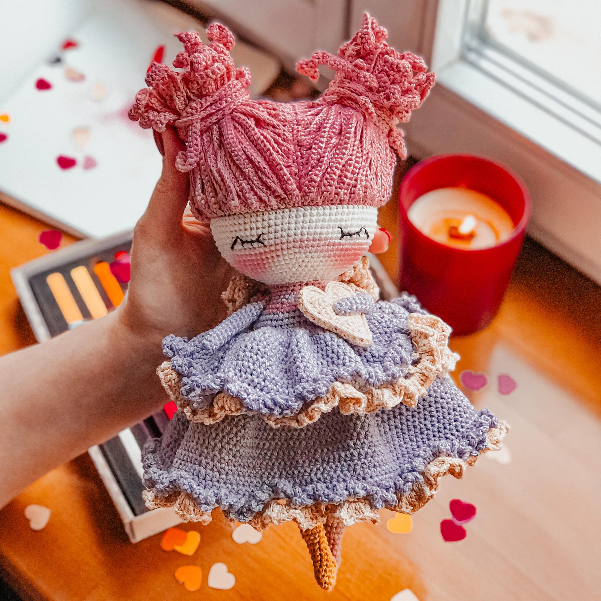 a hand holding a knitted doll on a table
