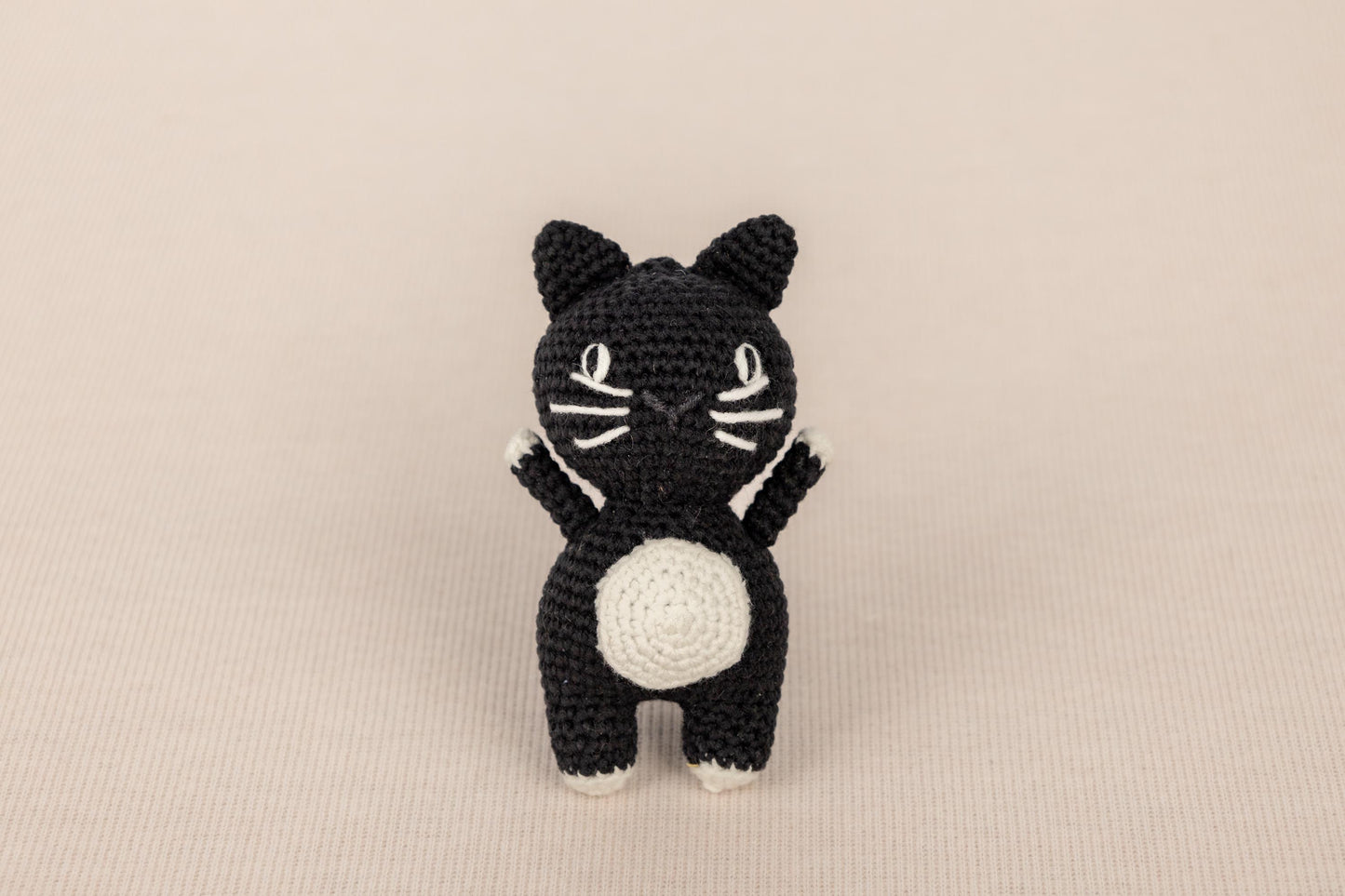 a crocheted black and white cat sitting on its hind legs