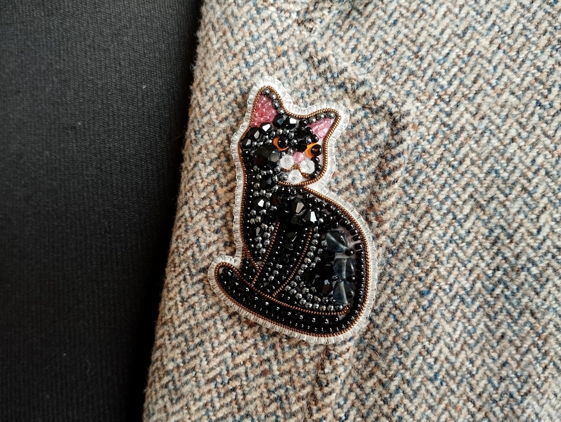 A close-up image of a decorative cat embroidered on a fabric, with a dark background.