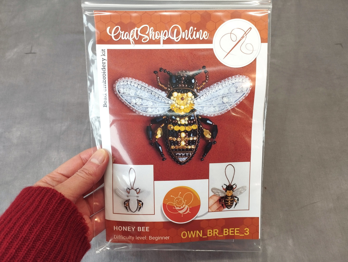 A hand holding a package containing a kit for creating a beehive embroidery piece.
