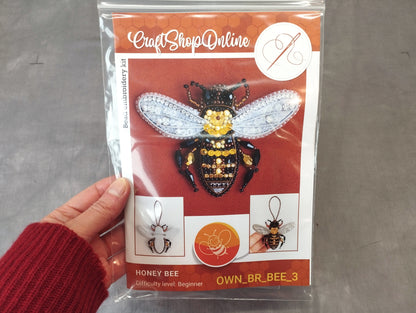 A hand holding a package containing a kit for creating a beehive embroidery piece.
