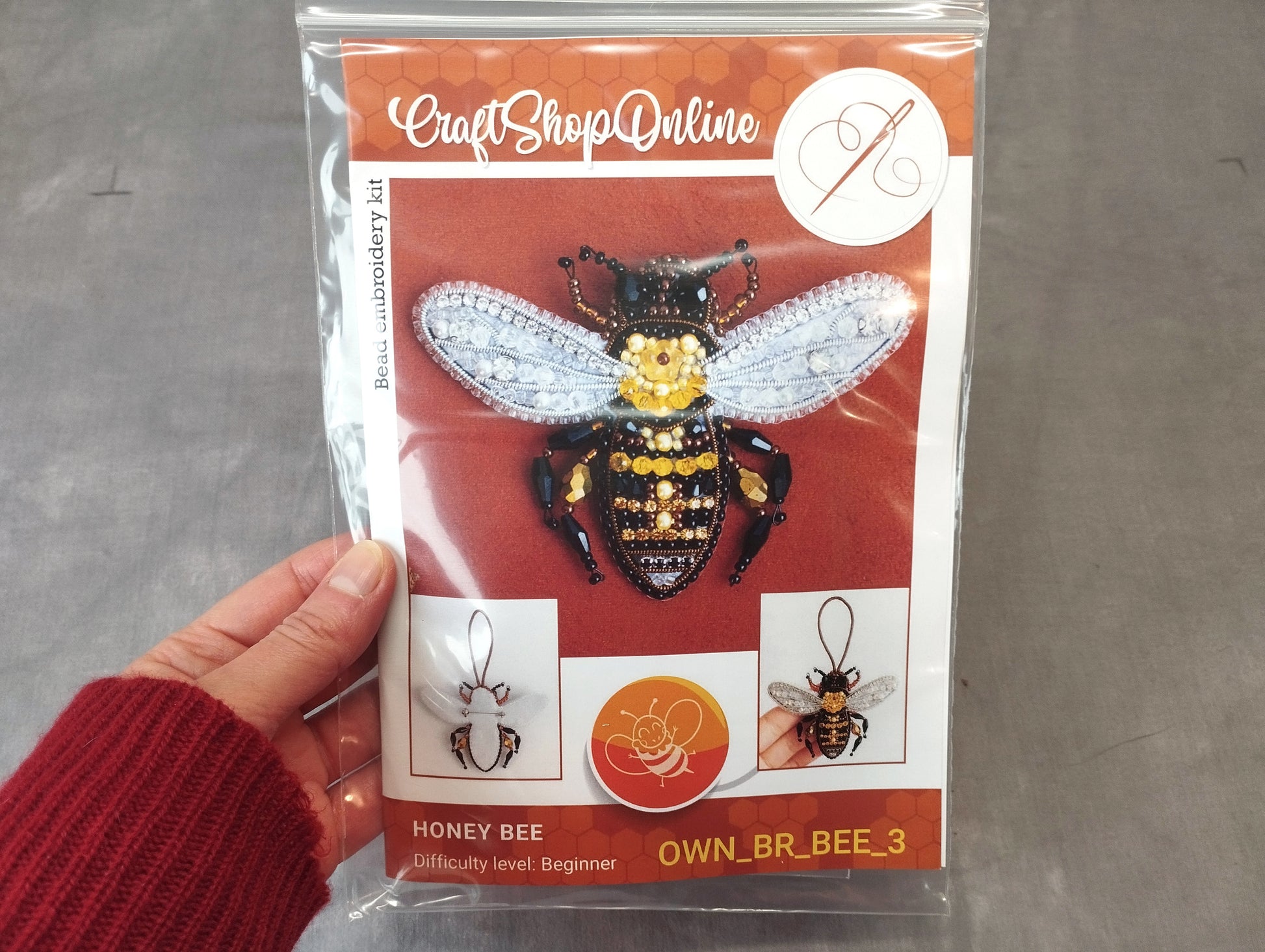 A hand holding a package containing a kit for creating a beehive embroidery piece.