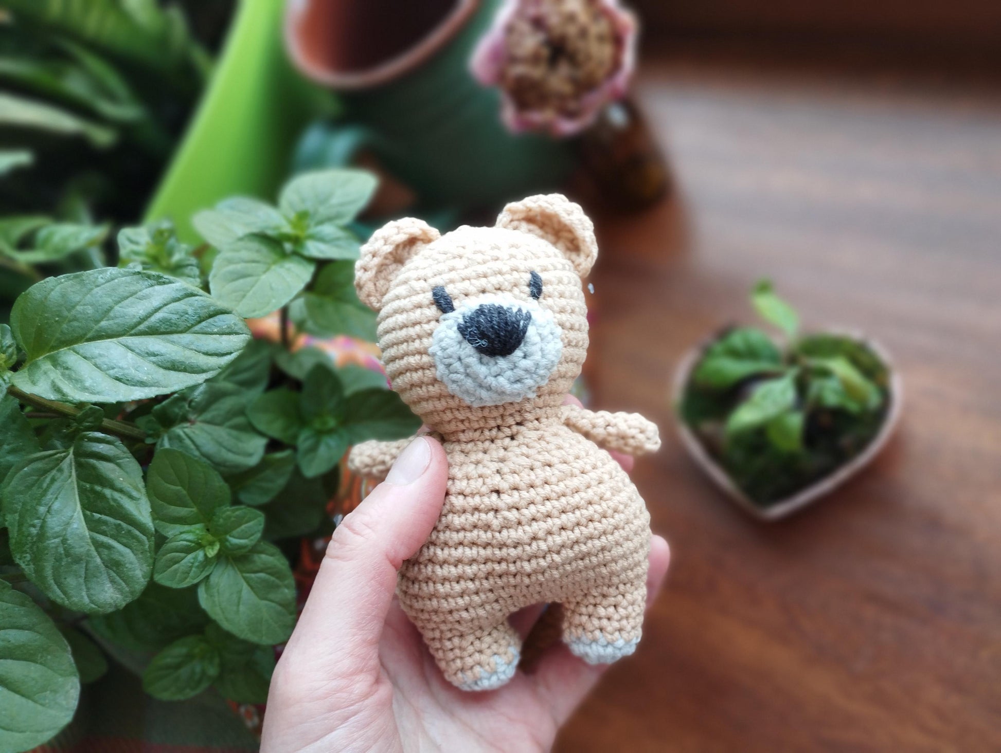 a hand holding a small crocheted teddy bear