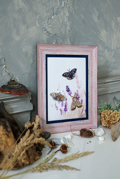 a framed painting of butterflies on a white background, surrounded by various natural elements such as dried flowers, rocks, and a wooden log.