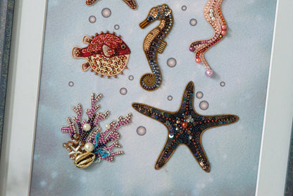 a collection of colorful, intricately designed sea creatures, including a red fish, a brown seahorse, a purple starfish, and a black starfish, all adorned with beaded and embroidered embellishments.