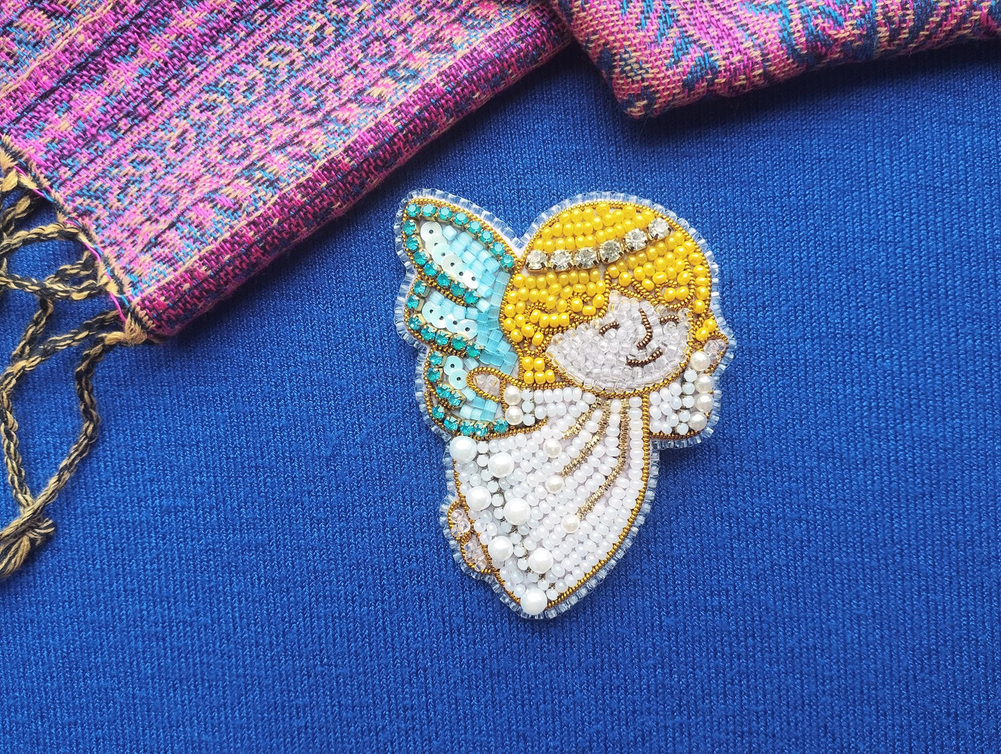 a close-up view of a beaded embroidered figure of an angel on a blue background.