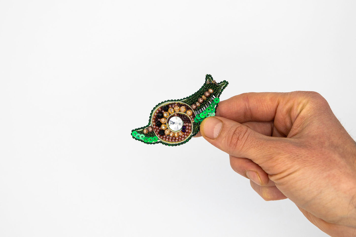 a hand holding a green and brown brooch