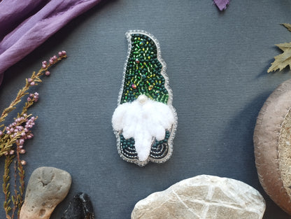 a close-up of a decorative item, possibly a brooch or pin, with a green and white color scheme and a white feather at the center. The item is surrounded by various natural elements, such as rocks, leaves, and flowers, creating a harmonious and visually appealing composition.