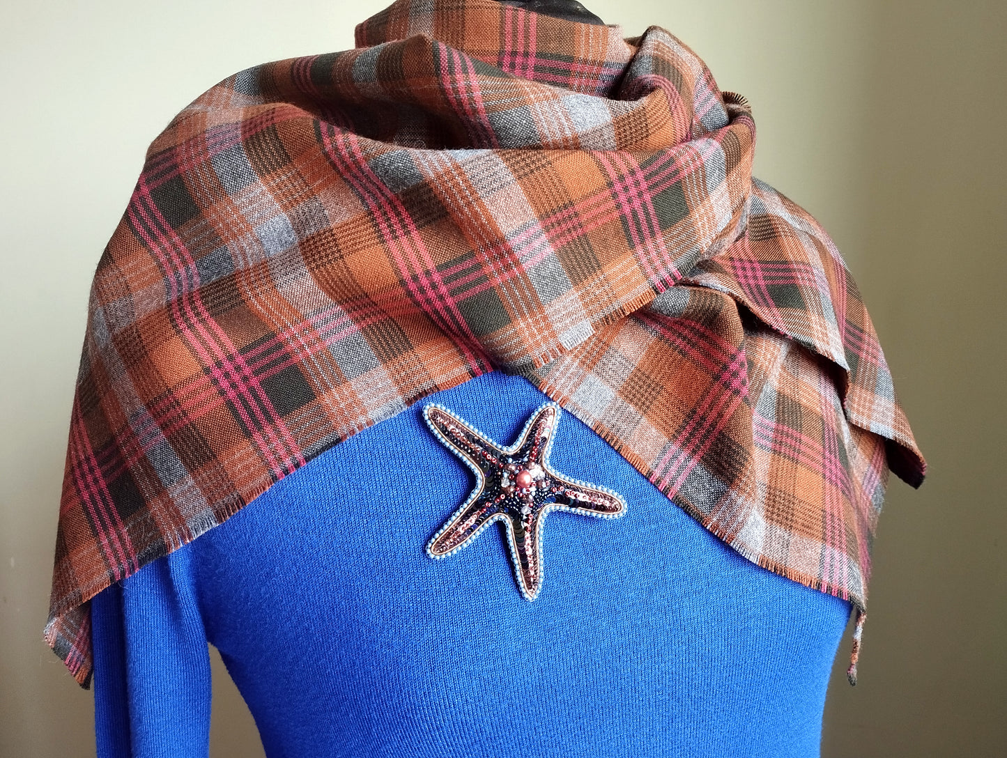 A plaid scarf is draped over a blue sweater, with a starfish brooch pinned to the sweater.