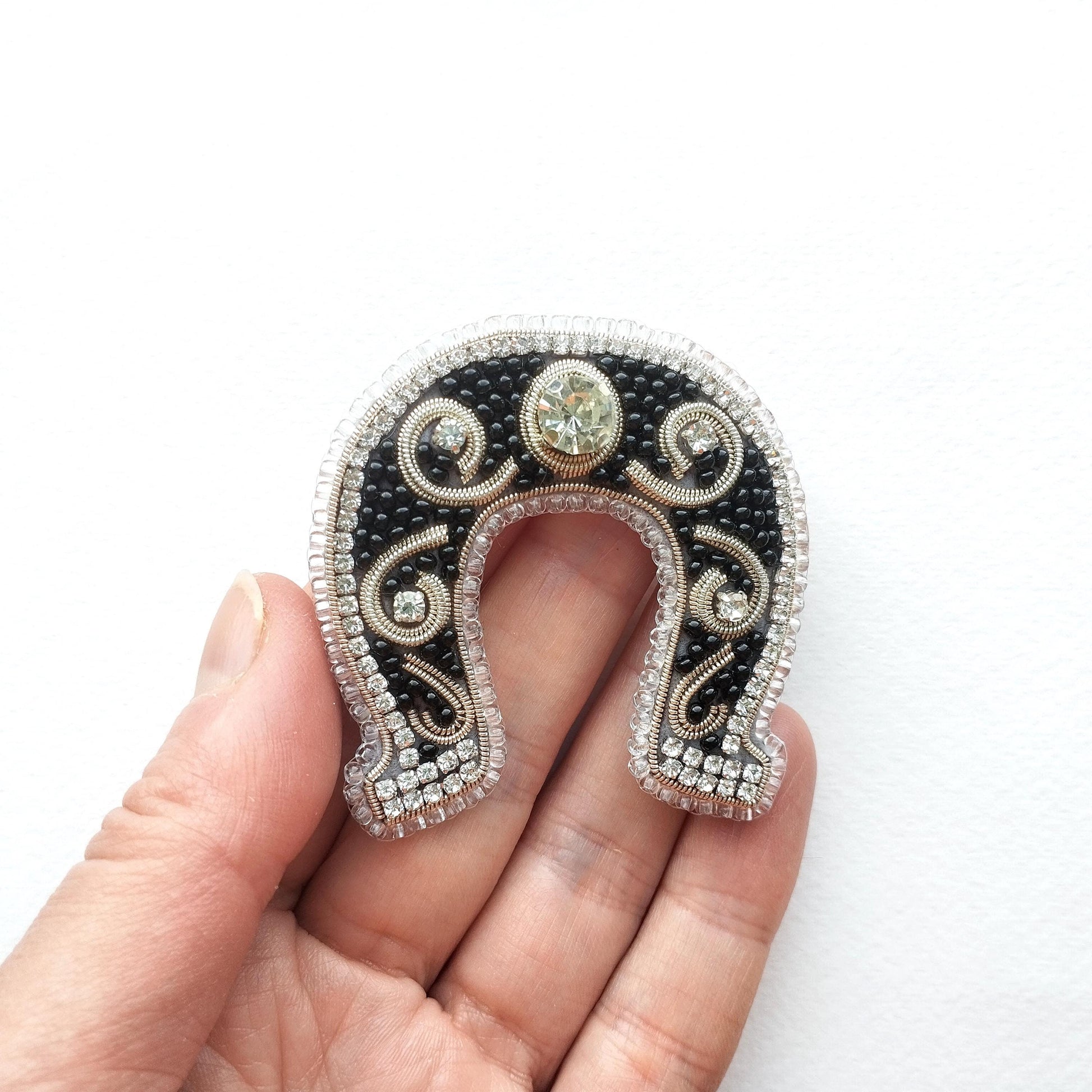 A hand holding a decorative horseshoe-shaped piece of jewelry with a black background, silver and gold accents, and a central gemstone.