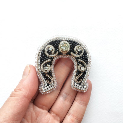 A hand holding a decorative horseshoe-shaped piece of jewelry with a black background, silver and gold accents, and a central gemstone.