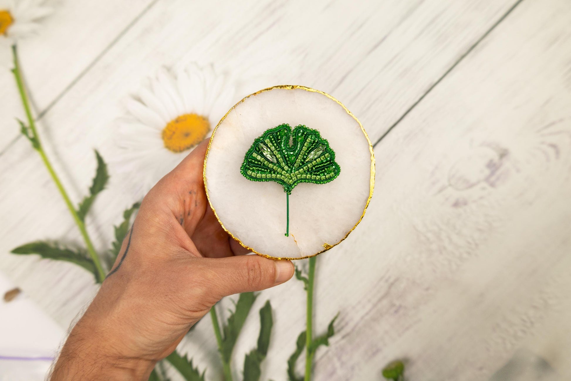 a hand holding a small green leaf on a white surface