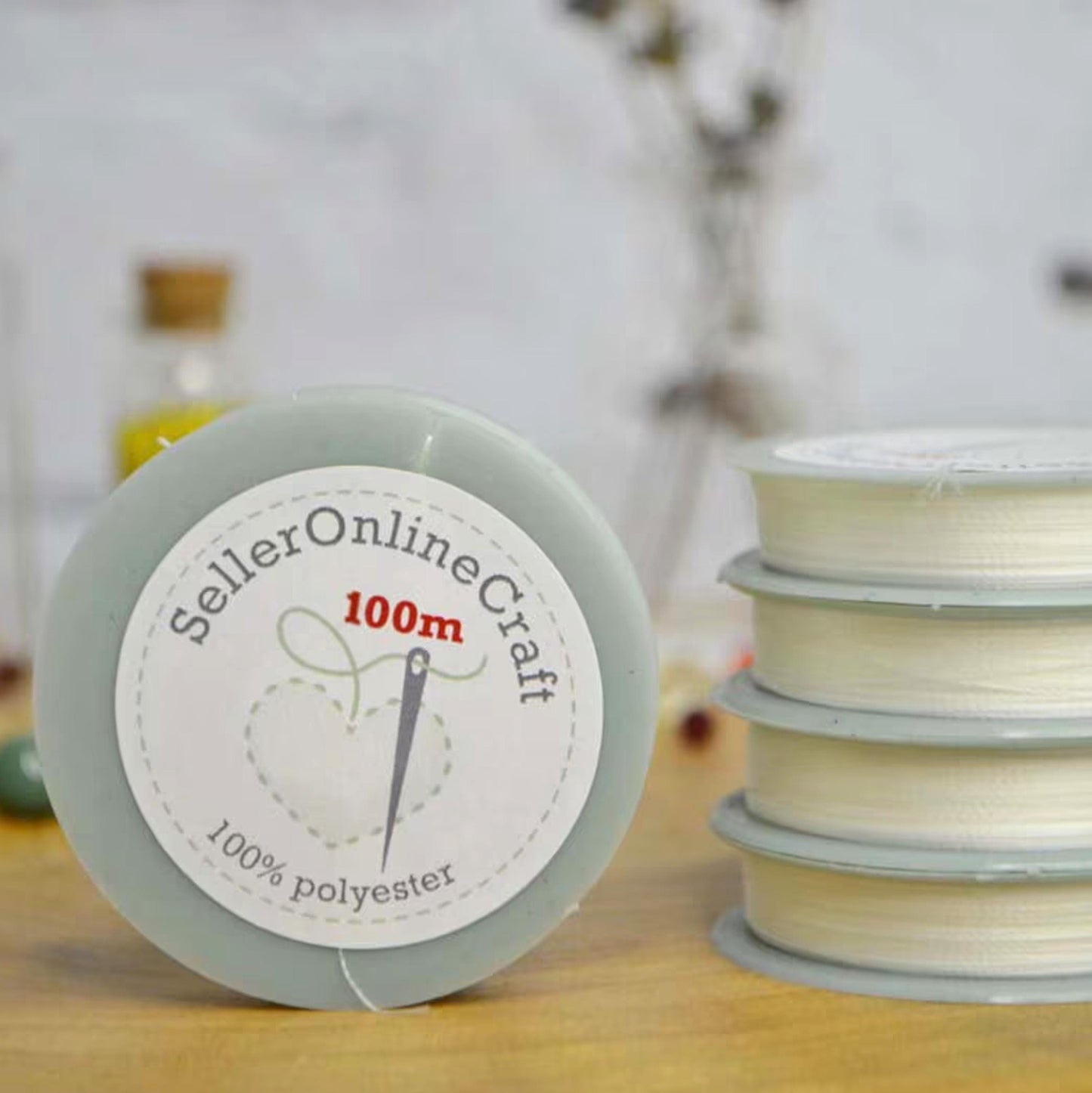 a close-up of a spool of thread labeled "Seller Online Craft 100m 100% polyester" on a table, with a stack of similar spools visible in the background.
