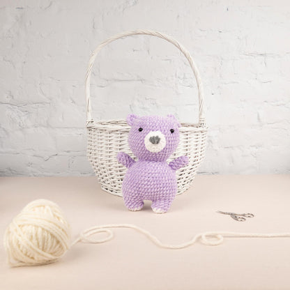 a purple teddy bear sitting next to a ball of yarn