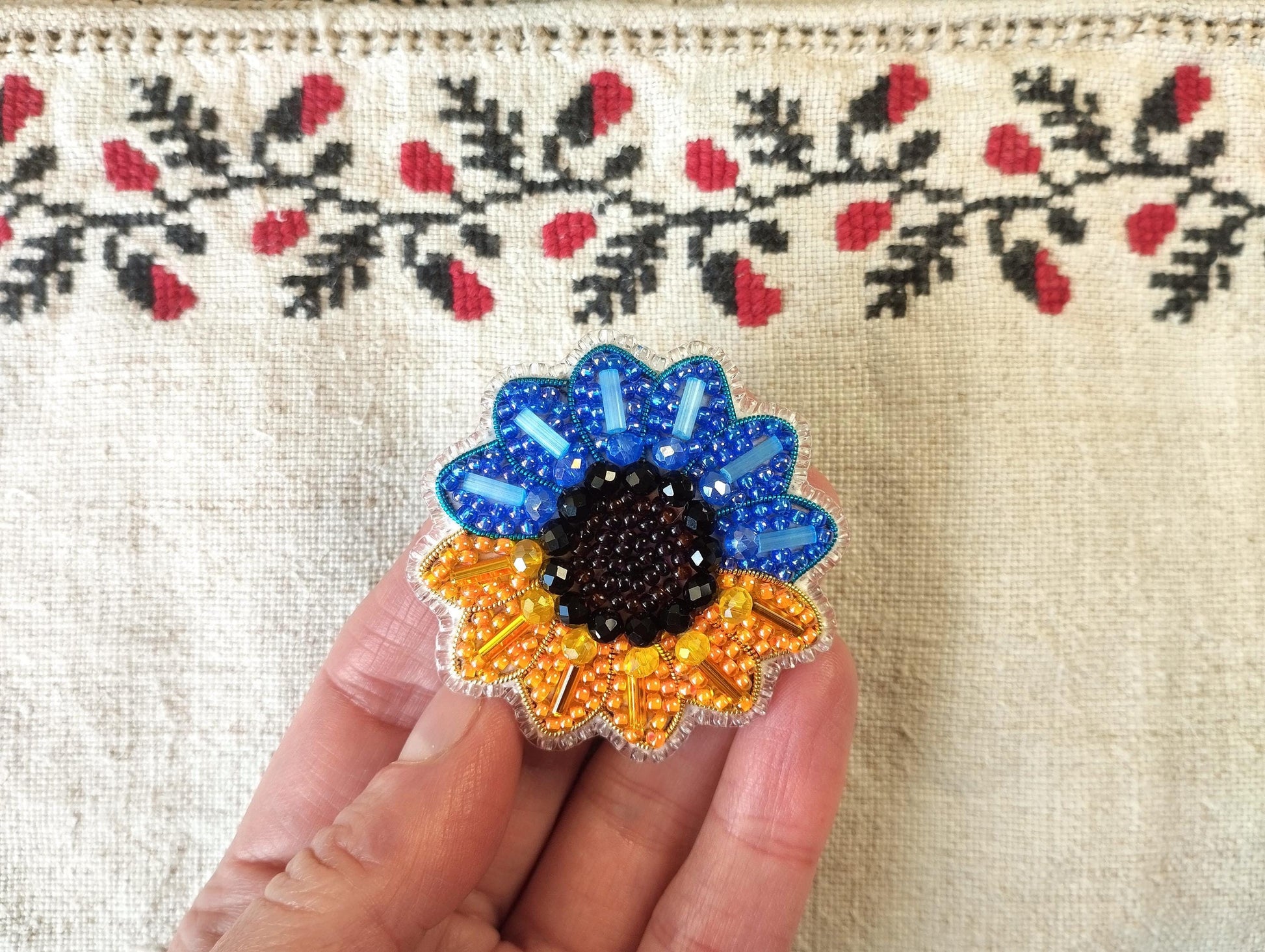 A hand holding a colorful beaded flower-shaped pin against a background with a floral pattern.