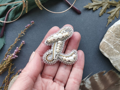 A hand holding a decorative letter 'L' made of beads and pearls against a dark background.