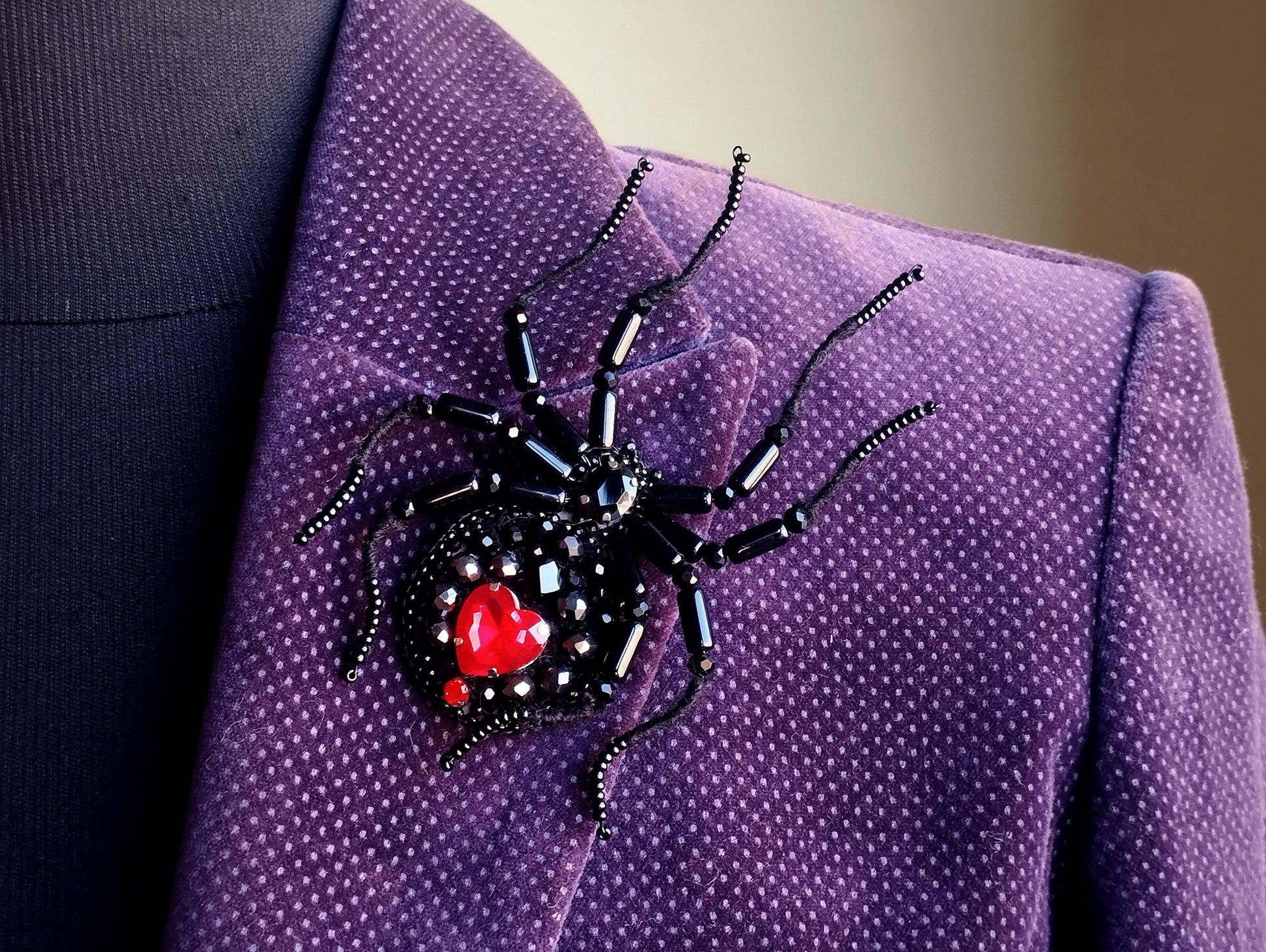 A close-up view of a purple jacket with a black spider-shaped brooch featuring a red heart in the center.