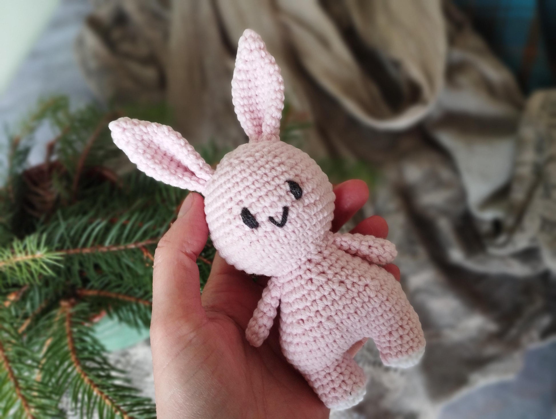 a hand holding a small pink crocheted bunny
