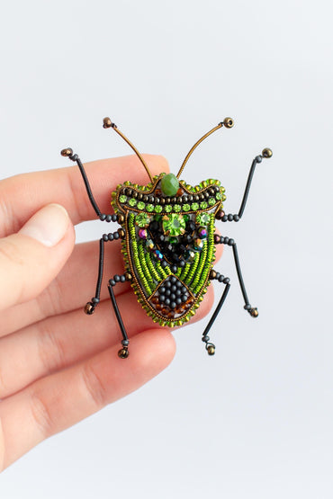 a hand holding a green beaded bug on a white background