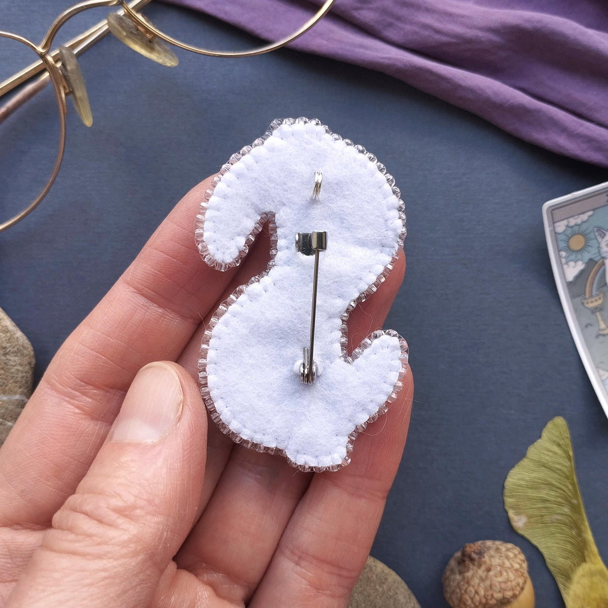 A hand holding a white felt pin shaped like a dollar sign, with a pinback attached to it.