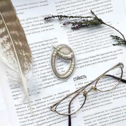 a close-up of a page with text in Russian, accompanied by a pair of glasses, a feather, and a necklace with a pendant.