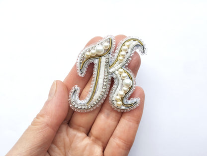 A hand holding a decorative letter 'K' made of beads, pearls, and rhinestones.