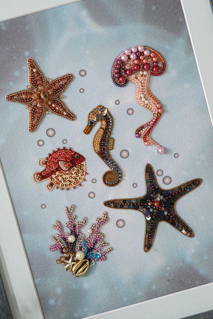 a collection of six decorative sea-themed objects, including a starfish, a seahorse, a jellyfish, a pearl, a coral, and a starfish, all adorned with colorful beads and sequins.