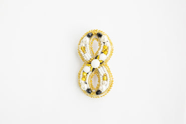 a yellow and white beaded brooch on a white background
