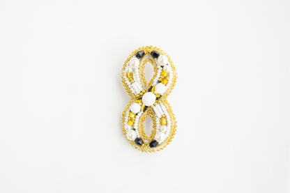 a yellow and white beaded brooch on a white background