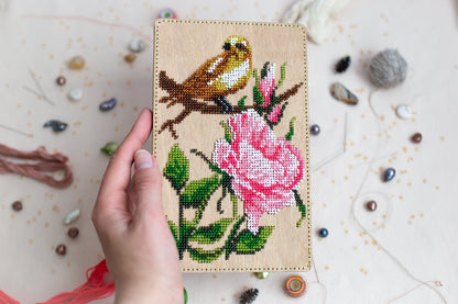 a hand is holding a cross stitch picture of a bird on a branch