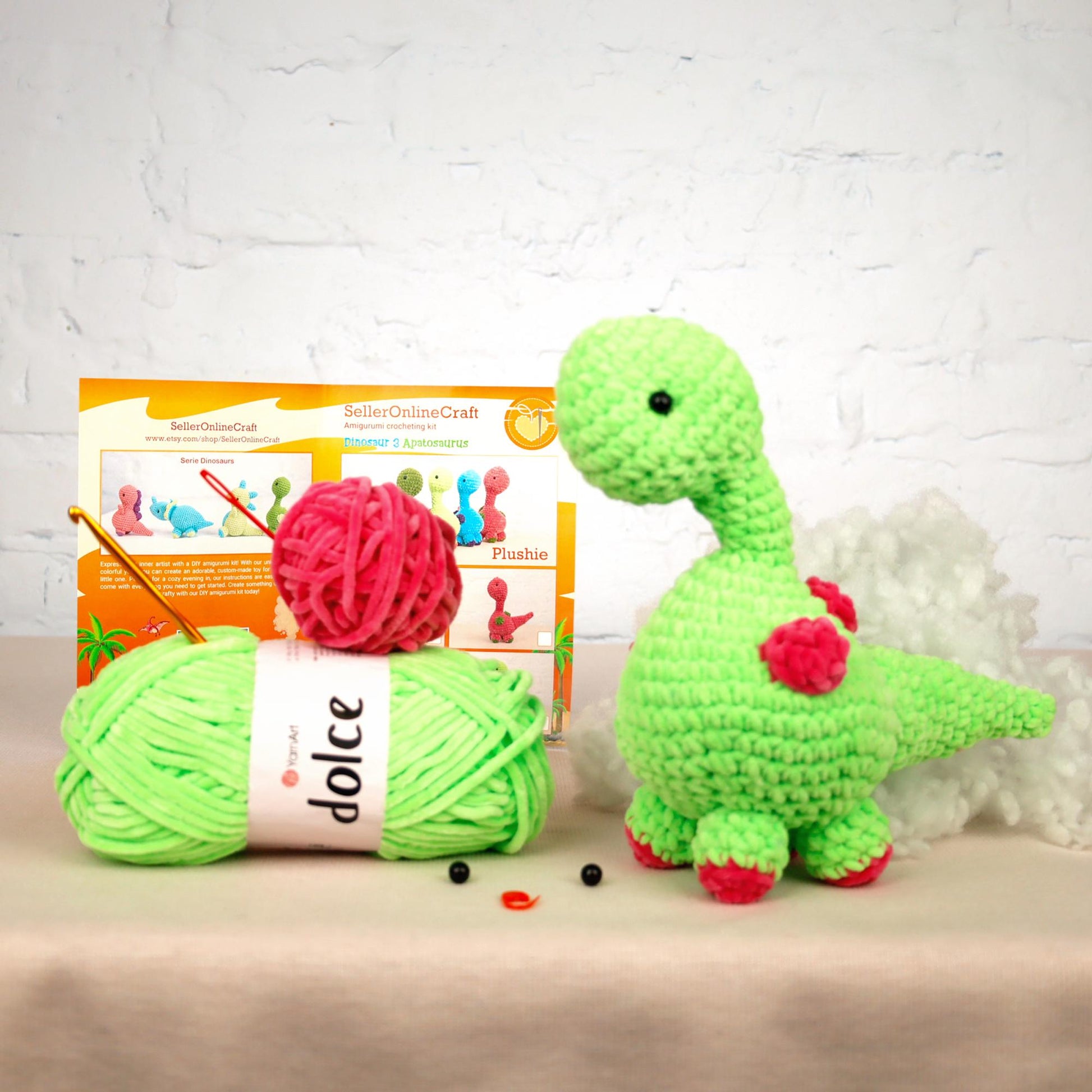 a green crochet dinosaur next to a ball of yarn