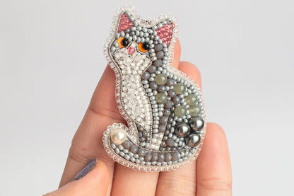 A hand holding a decorative cat pin made of beads and pearls.