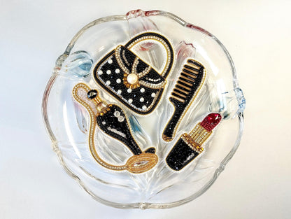 A glass plate with various decorative items, including a handbag, comb, and lipstick, arranged on it.