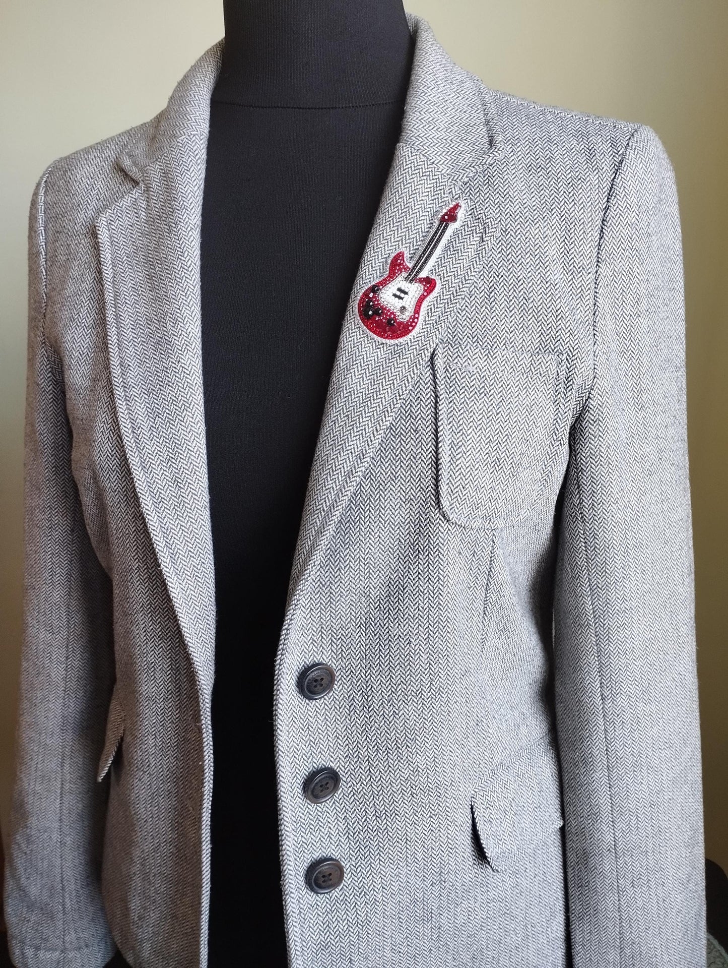 A gray tweed jacket with a red guitar patch on the left breast pocket.