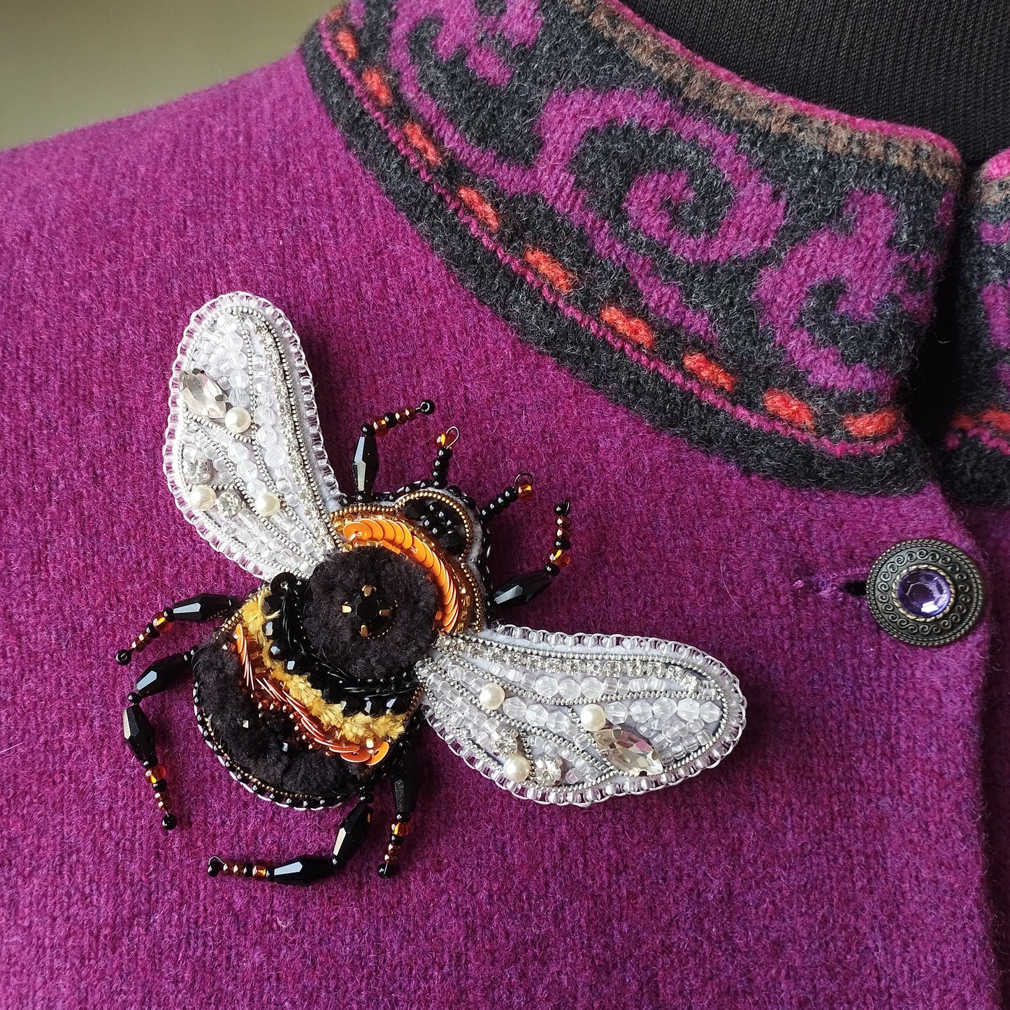 A close-up image of a purple sweater with a detailed, hand-made beaded bee embroidered on it.