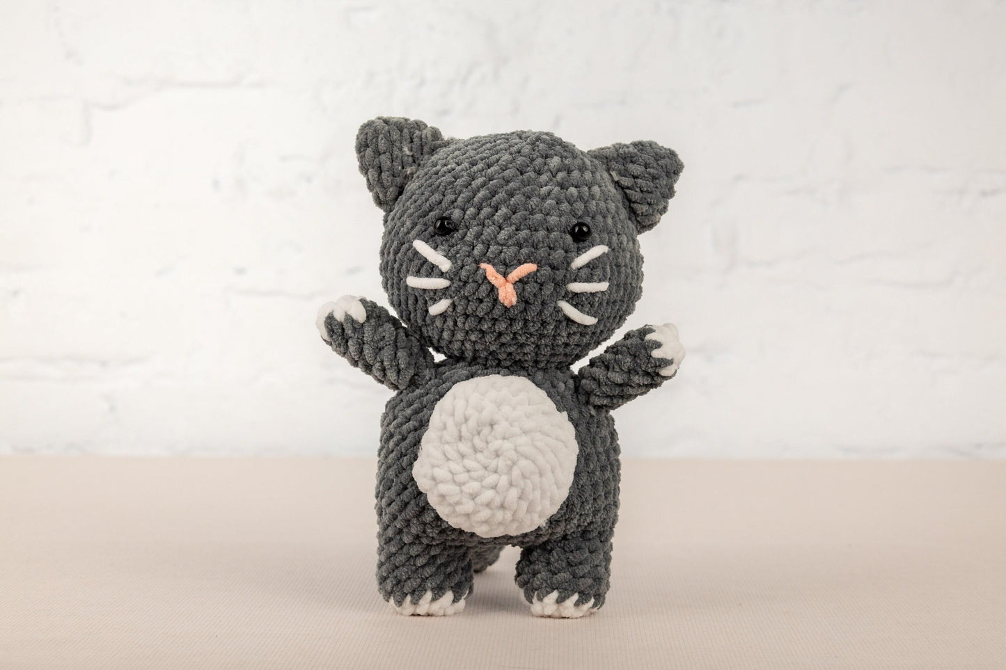 a crocheted black and white cat holding a white ball