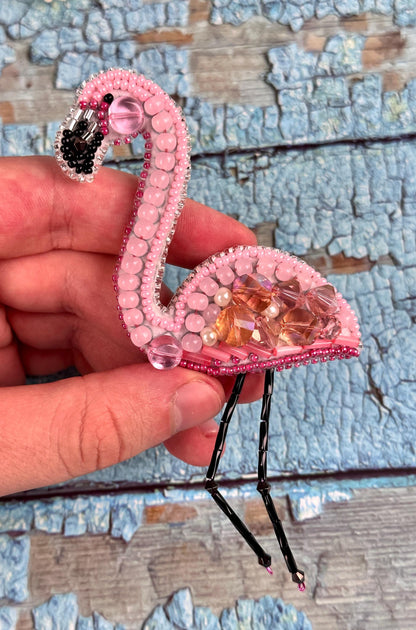 a hand holding a pink flamingo brooch