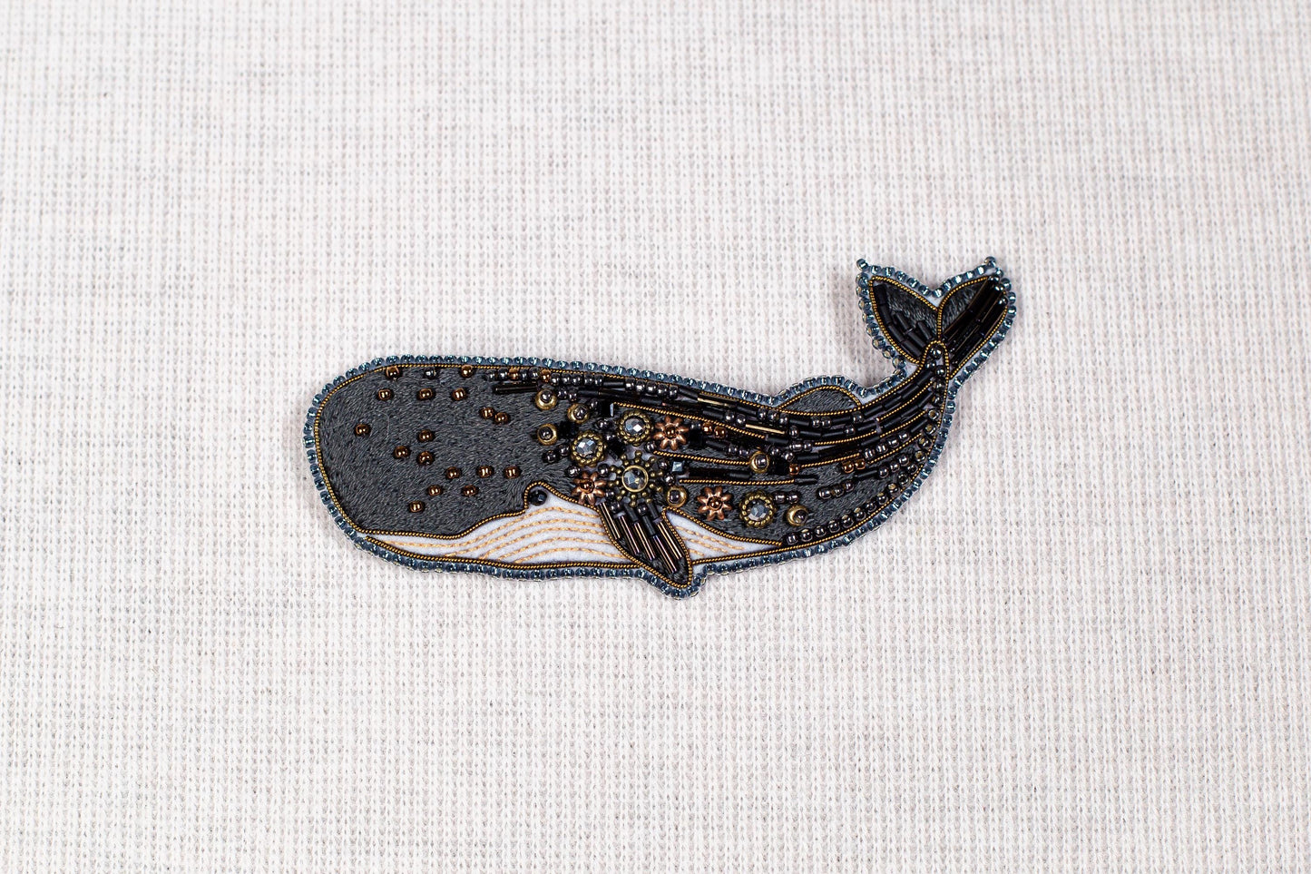 a detailed embroidered or beaded whale design on a plain white background.
