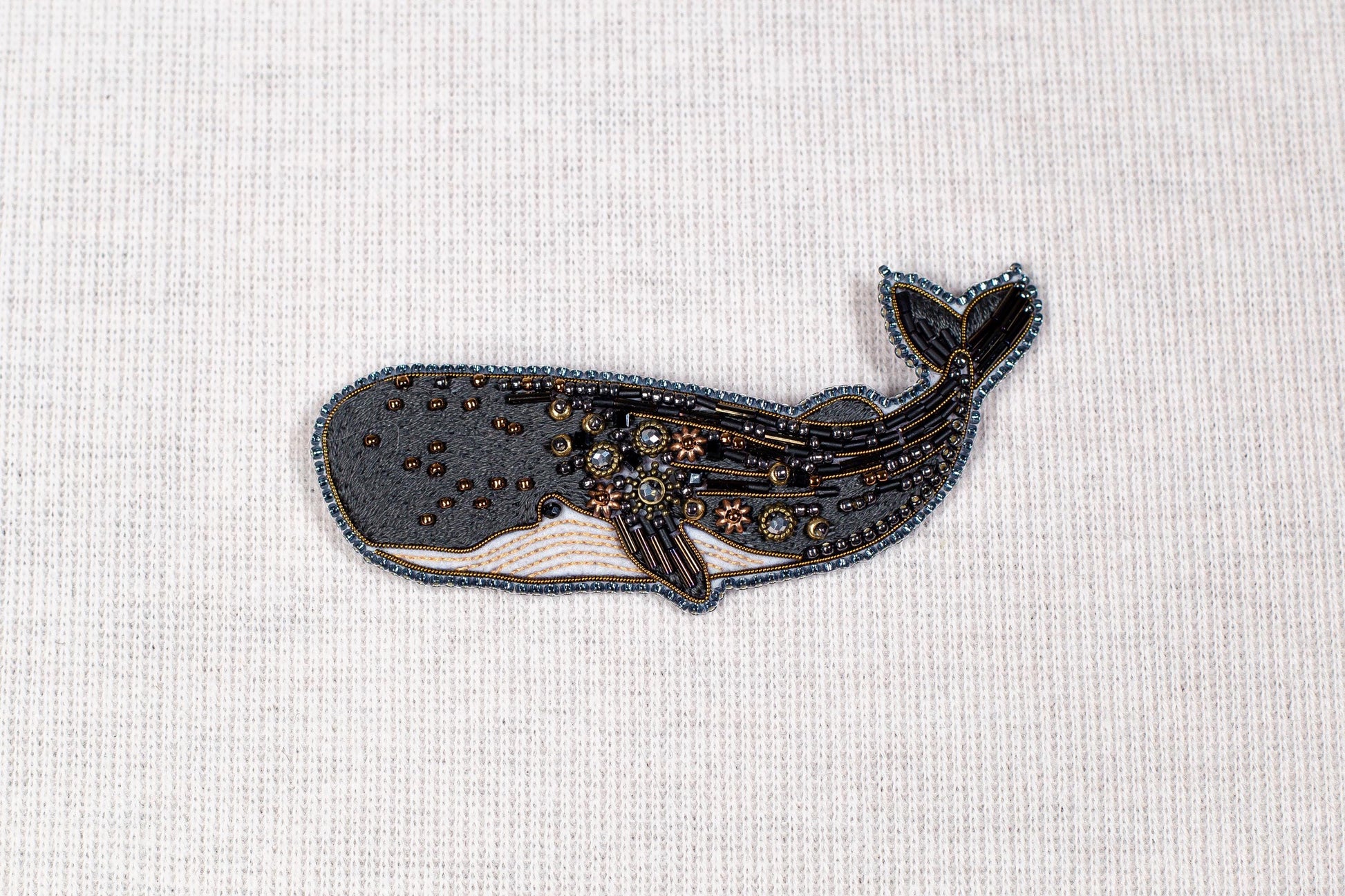a detailed embroidered or beaded whale design on a plain white background.