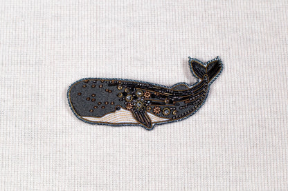 a detailed embroidered or beaded whale design on a plain white background.