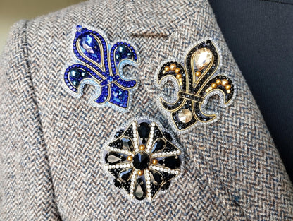 a close-up view of a grey tweed jacket with three decorative brooches or pins attached to it.