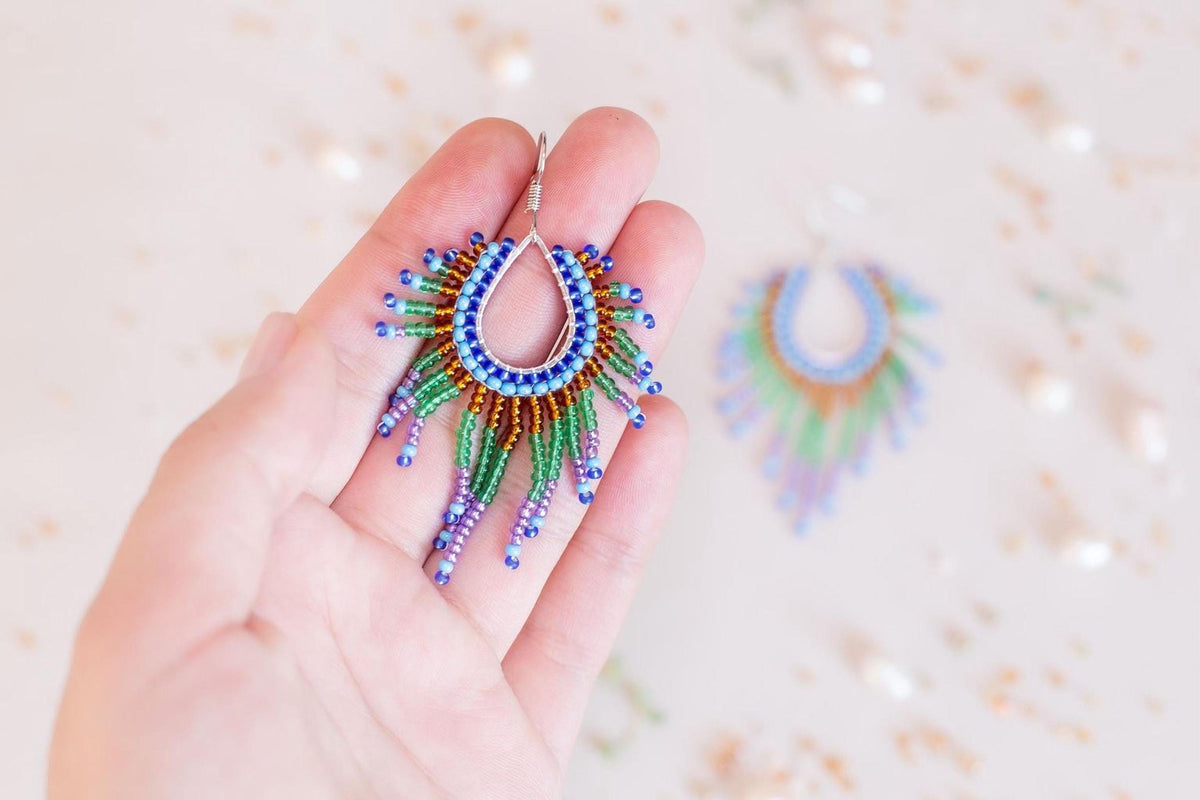 A hand holding a pair of colorful earrings with blue, green, and purple beads.