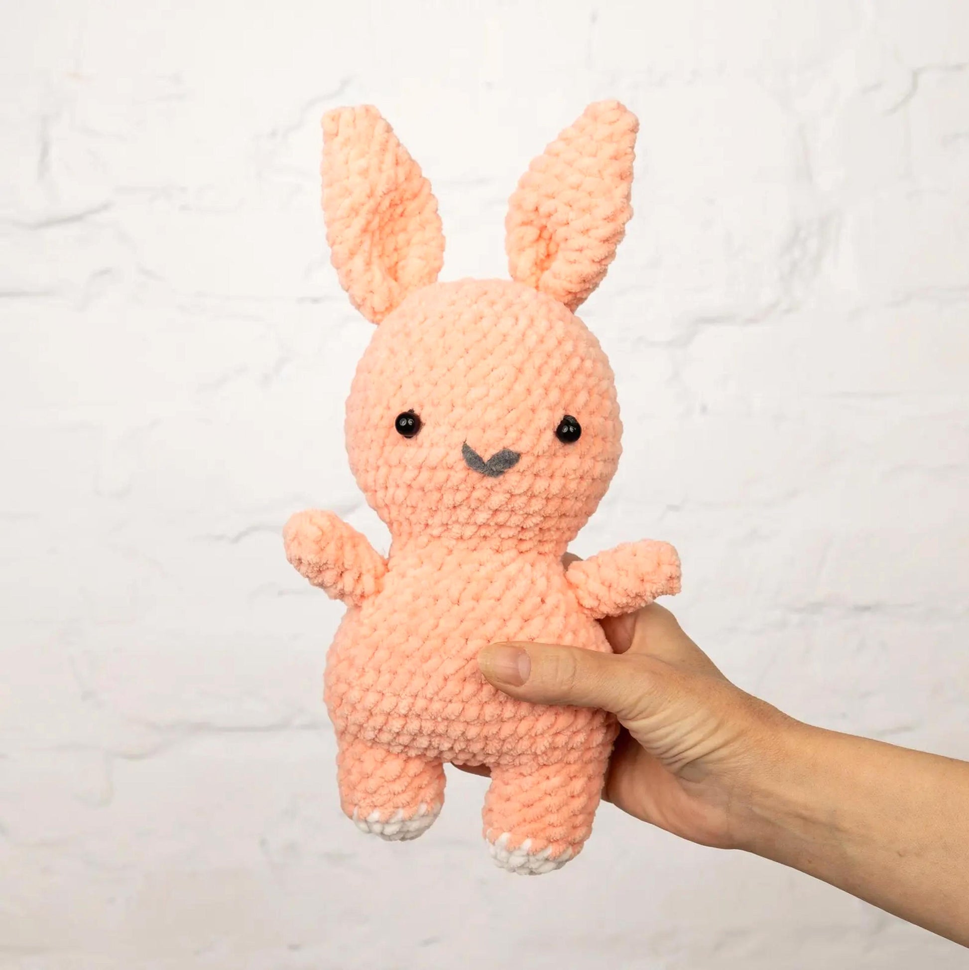 A hand is holding a small, crocheted pink bunny toy against a white background.