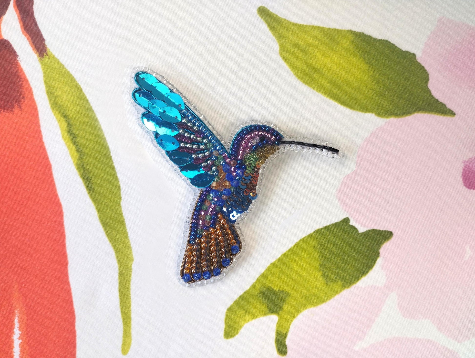 a colorful bird brooch sitting on top of a flowered surface