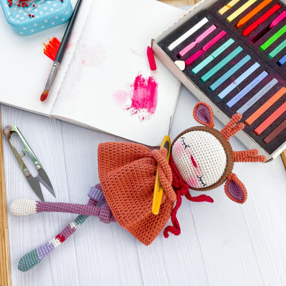 a crocheted doll next to a crayon book and crayons