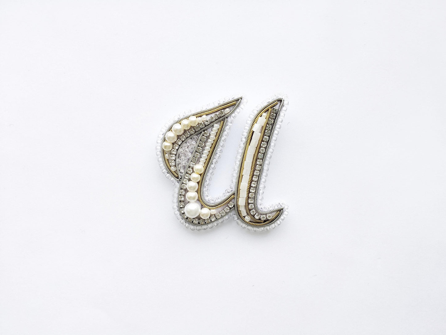 A decorative letter 'U' made of beads, pearls, and crystals against a white background.