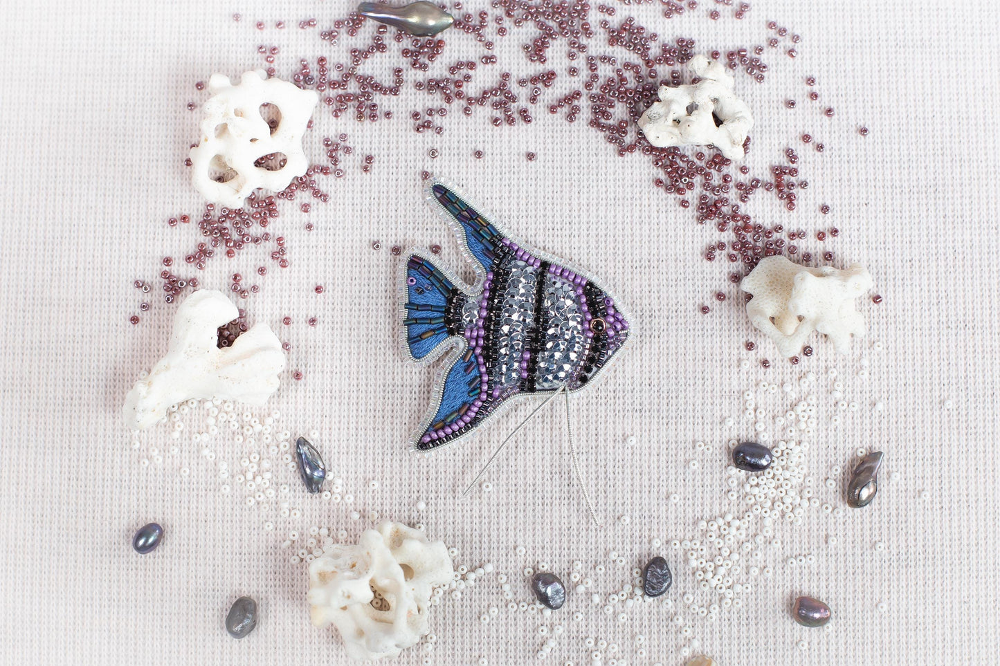 a blue and purple fish surrounded by various sea-themed objects, including pearls, coral, and beads, all arranged on a white background.