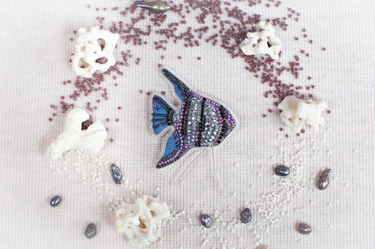 a blue and purple fish surrounded by various sea-themed objects, including pearls, coral, and beads, all arranged on a white background.