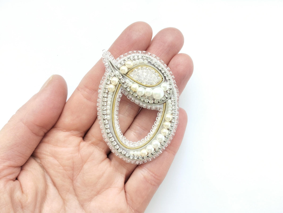 A hand holding a decorative piece of jewelry, which appears to be a brooch or pendant.
